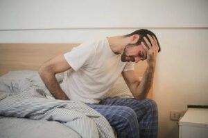 man not feeling well sitting on his bed